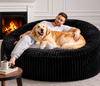 Man and dog relaxing on a large black pet bed in a cozy living room.