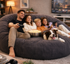 Family of four with a dog on a large bean bag in a living room.